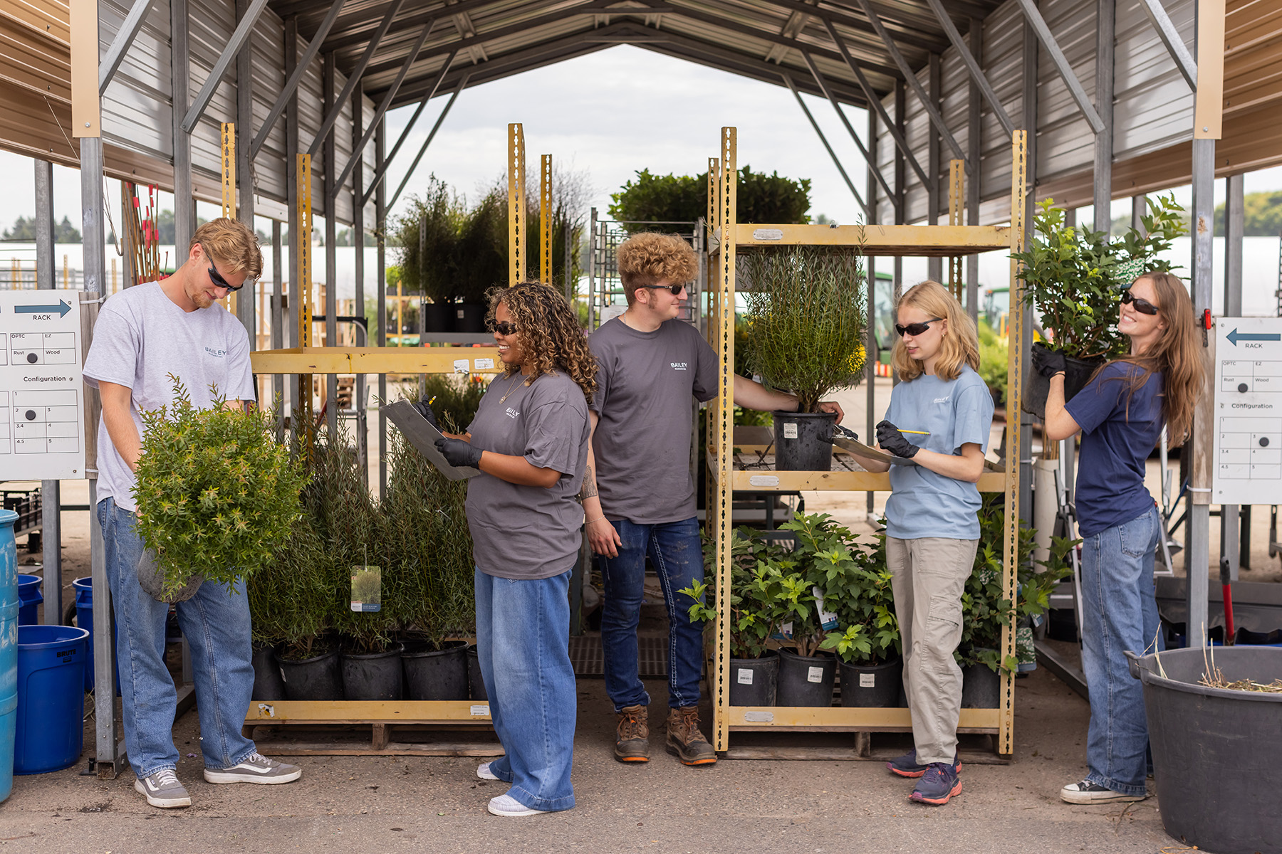 Interns at Container East stage and check potted shrubs on shipping racks.