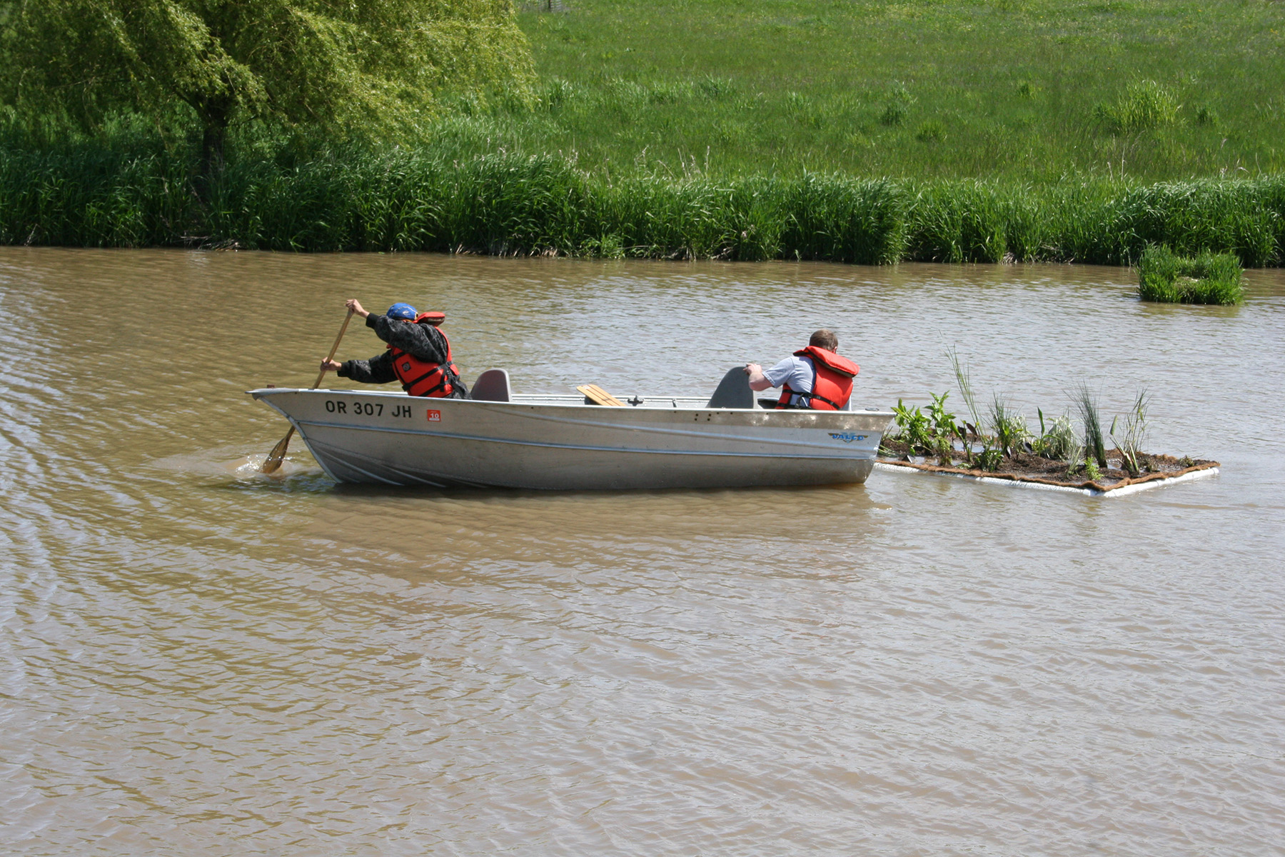 Bailey Nurseries staff in a small boat towing a planted floating island across an irrigation pond.